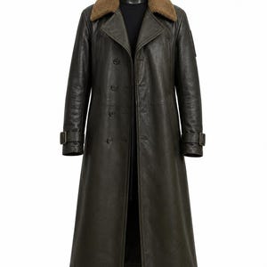 Op de afbeelding: Een donker olijfgroene leren trenchcoat met een bruine imitatiebontkraag, een dubbele rij knopen aan de voorzijde en verstelbare gespriemen bij de manchetten. De lange jas heeft een gestructureerd silhouet met brede revers en lange mouwen.