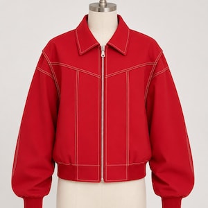 May include: A bright red jacket with a collar and a full zip. The jacket has white stitching detail and ribbed cuffs and hem. The sleeves are long and slightly puffed. The jacket is displayed on a mannequin.