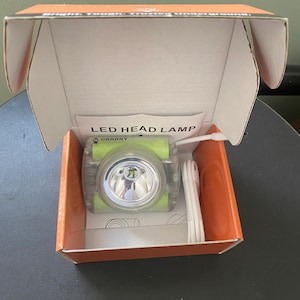 May include: An LED head lamp in an orange box. The headlamp is green and clear with a bright light. The box also contains a white USB cable and a small instruction sheet. The text "LED HEAD LAMP" is printed on the box.