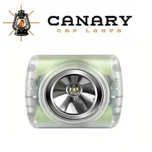 May include: A rectangular cap lamp with a translucent white casing and a central circular silver reflector housing a single LED light. Above the lamp, the text CANARY CAP LAMPS appears in black and orange, accompanied by a lantern icon.