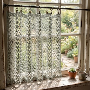 May include: A pale sage green crochet curtain featuring an intricate openwork net pattern with vertical columns of teardrop-shaped motifs. The curtain is suspended from a dark metal rod by eight matching metal clips, creating soft, uniform folds.