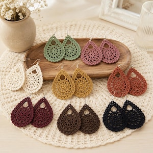 Puede incluir: Una colección de pendientes de ganchillo en forma de lágrima en varios colores, incluyendo verde salvia, rosa empolvado, crema, amarillo mostaza, terracota, burdeos, marrón oscuro y negro. Cada par presenta un patrón de encaje circular.