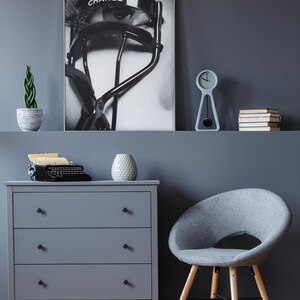 Puede incluir: Una impresi&oacute;n en escala de grises de un ojo con un rizador de pesta&ntilde;as CHANEL se muestra sobre una c&oacute;moda gris. Un peque&ntilde;o reloj, libros y una planta en maceta est&aacute;n en el estante. Una silla gris y una m&aacute;quina de escribir vintage tambi&eacute;n est&aacute;n en la habitaci&oacute;n.