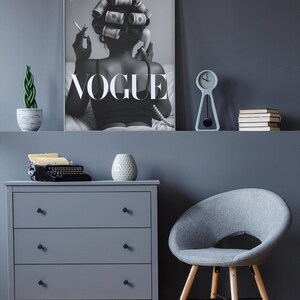 Puede incluir: Un p&oacute;ster en escala de grises de Vogue cuelga sobre una c&oacute;moda gris y una silla gris con patas de madera. Una peque&ntilde;a planta, un reloj y libros est&aacute;n en un estante. Una m&aacute;quina de escribir vintage y un jarr&oacute;n decorativo est&aacute;n en la c&oacute;moda.