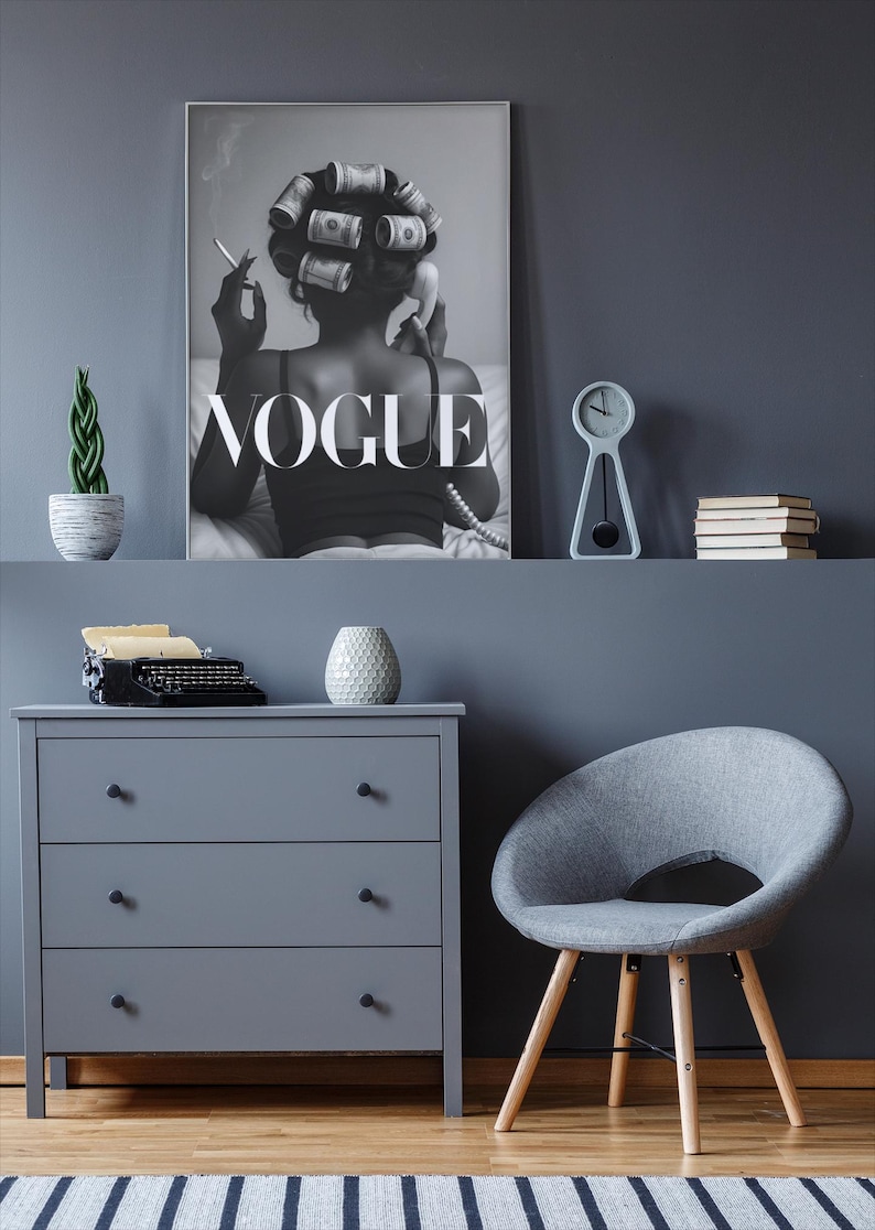 Puede incluir: Un p&oacute;ster en escala de grises de Vogue cuelga sobre una c&oacute;moda gris y una silla gris con patas de madera. Una peque&ntilde;a planta, un reloj y libros est&aacute;n en un estante. Una m&aacute;quina de escribir vintage y un jarr&oacute;n decorativo est&aacute;n en la c&oacute;moda.