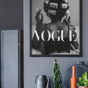Puede incluir: Impresi&oacute;n en blanco y negro enmarcada que presenta a una mujer con billetes de d&oacute;lar en el pelo, fumando un cigarrillo y sosteniendo un tel&eacute;fono antiguo. La palabra "VOGUE" se muestra de forma destacada. Objetos decorativos sobre una superficie gris.