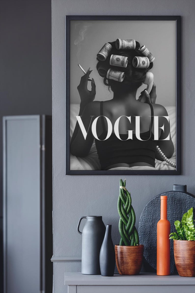 Puede incluir: Impresi&oacute;n en blanco y negro enmarcada que presenta a una mujer con billetes de d&oacute;lar en el pelo, fumando un cigarrillo y sosteniendo un tel&eacute;fono antiguo. La palabra "VOGUE" se muestra de forma destacada. Objetos decorativos sobre una superficie gris.