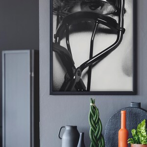 Puede incluir: Impresi&oacute;n enmarcada en blanco y negro de un ojo con largas pesta&ntilde;as y un rizador de pesta&ntilde;as Chanel. El rizador est&aacute; colocado sobre el ojo, con el nombre de la marca visible. Parte de una exhibici&oacute;n decorativa.