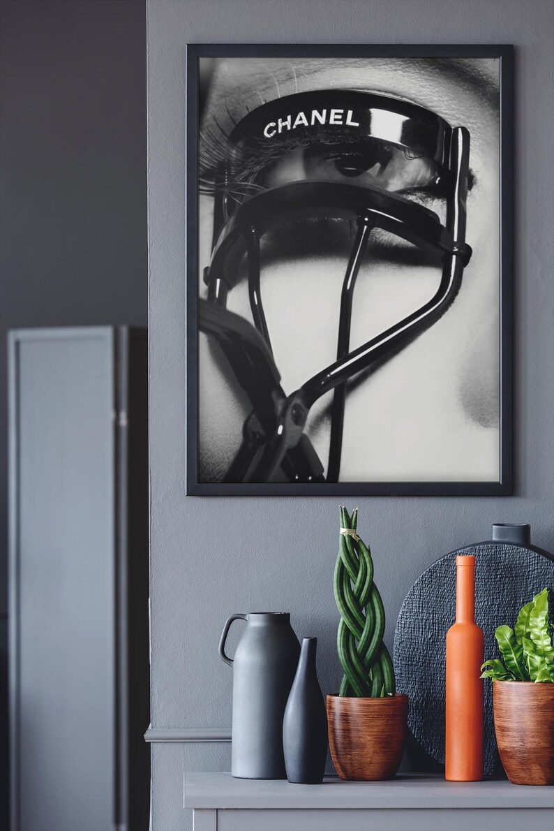 Puede incluir: Impresi&oacute;n enmarcada en blanco y negro de un ojo con largas pesta&ntilde;as y un rizador de pesta&ntilde;as Chanel. El rizador est&aacute; colocado sobre el ojo, con el nombre de la marca visible. Parte de una exhibici&oacute;n decorativa.