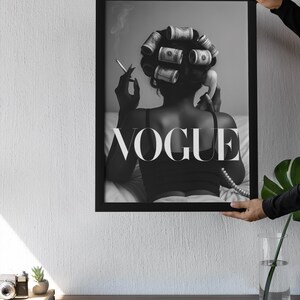 Puede incluir: Impresi&oacute;n en blanco y negro enmarcada que muestra a una mujer con rulos de dinero, fumando un cigarrillo y usando un tel&eacute;fono antiguo. La palabra "VOGUE" se muestra. La impresi&oacute;n es sostenida por una persona.