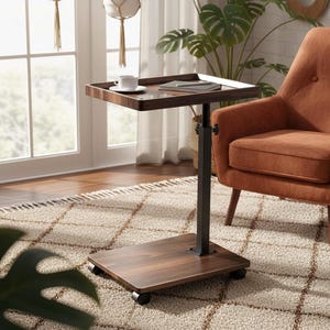 May include: A dark brown, adjustable height side table with a square top and a rectangular base on wheels. A white teacup and saucer sit on the table, next to a book. An orange armchair is in the background.