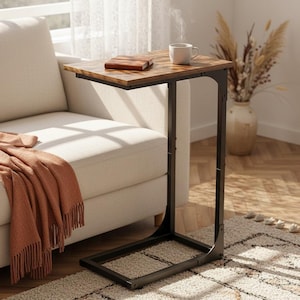 May include: A brown and black side table with a rectangular top and a black metal frame. A white mug, a brown book, and a small brown leather-bound notebook sit on the table. A peach-colored blanket is draped over a white sofa.