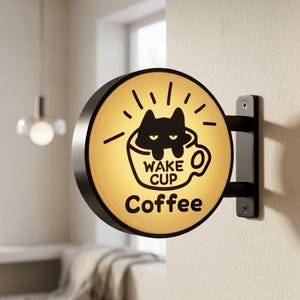 Könnte beinhalten: Rundes, beleuchtetes Kaffeeladenschild mit einer schwarzen Katze in einer Kaffeetasse. Der Schriftzug lautet "WAKE CUP Coffee" in einer verspielten Schriftart. Das Schild ist an einer schwarzen Metallhalterung befestigt.