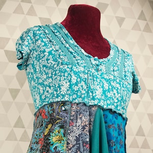May include: A turquoise blue and green patchwork top with a floral print. The top has a ruffled neckline and a flowing, asymmetrical hem.