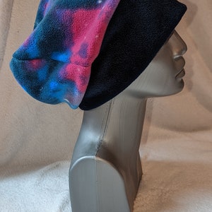 Può includere: Un berretto in pile nero e blu con stampa galassia. Il berretto è ripiegato verso il basso e ha una fodera in pile nera.