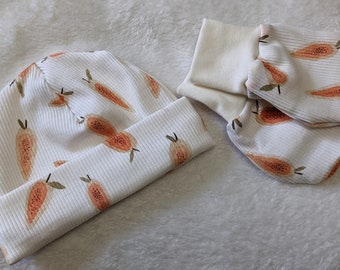 May include: White baby hat and mittens with a papaya print. The hat is folded and the mittens are laid out flat.