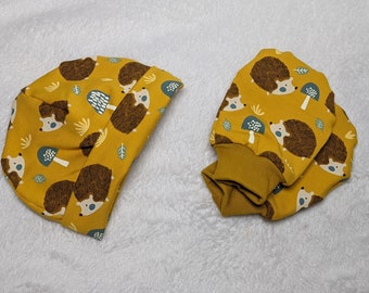May include: A set of two yellow fabric hats with a hedgehog and mushroom pattern. The hats are made of a soft, comfortable material and are perfect for keeping warm in the winter.