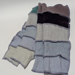 May include: A multi-coloured knitted scarf with a layered, ruffled design. The scarf is made of different shades of blue, grey, and brown.