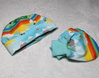 May include: A set of baby accessories featuring a blue and green hat and matching mittens. The fabric has a colourful rainbow, sun, and mountain design.