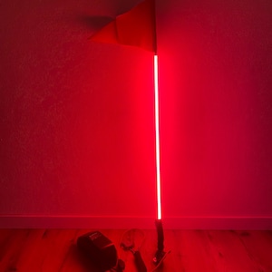 May include: A red LED whip with a red flag at the top. The light is on, illuminating the entire room in red. A black box and two tools are at the base of the whip.