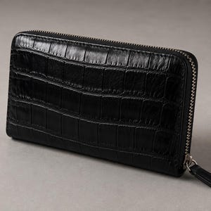 May include: Black, rectangular wallet with a textured, crocodile-like pattern. The wallet has a silver zipper closure that runs around three sides. The zipper pull is black. The wallet is on a gray surface.
