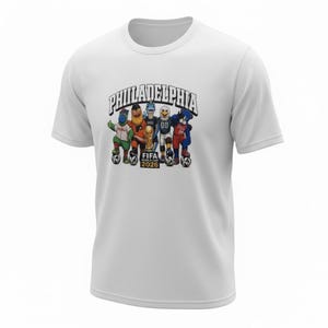 May include: White t-shirt featuring a graphic of Philadelphia mascots with a soccer ball, the FIFA World Cup trophy, and the text "Philadelphia FIFA World Cup 2026". The design includes various cartoon characters.