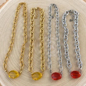 May include: Four chain necklaces with textured oval links. Two necklaces are gold-toned with yellow translucent oval pendants, and two are silver-toned with red translucent oval pendants. Each necklace features a lobster clasp and an extender chain.