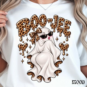 May include: A white t-shirt featuring a graphic of a ghost wearing black sunglasses and a leopard print bow. The text BOO-JEE is written in a dripping leopard print font above the ghost, flanked by two leopard print hearts and small stars.