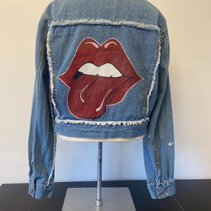 Med to light wash denim jacket, raw edges, Red Lips on back and small patch on front
