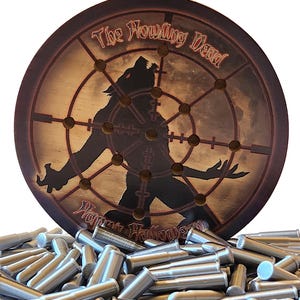 May include: A circular wooden target board featuring a silhouette of a werewolf, a crosshair design, and the text "The Howling Dead" and "Happy Halloween," resting on a pile of numerous small, silver-colored metal bullet-shaped pegs.