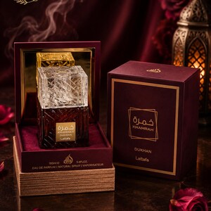 May include: A 100ml bottle of Lattafa Khamrah Dukhan Eau de Parfum with a clear, textured glass cap and a dark amber base. The bottle sits in an open, deep red velvet-lined box next to its matching rectangular box, both featuring gold text.