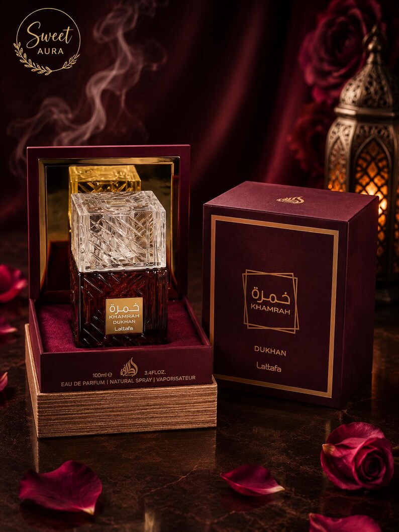 May include: A 100ml bottle of Lattafa Khamrah Dukhan Eau de Parfum with a clear, textured glass cap and a dark amber base. The bottle sits in an open, deep red velvet-lined box next to its matching rectangular box, both featuring gold text.
