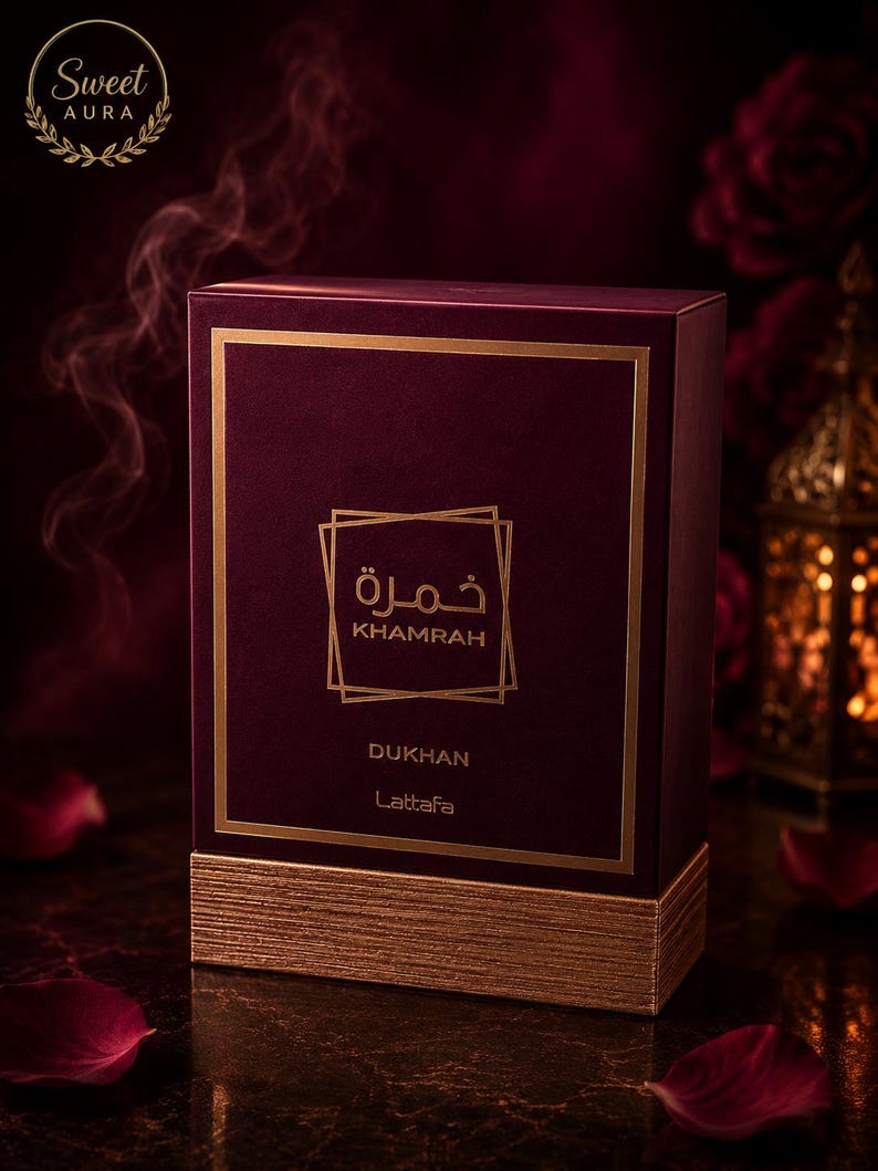 May include: A rectangular deep burgundy perfume box with a textured gold base. The front features gold-colored text reading Khamrah and Dukhan, along with the brand name Lattafa, enclosed in a gold square frame. The top left corner displays a logo.