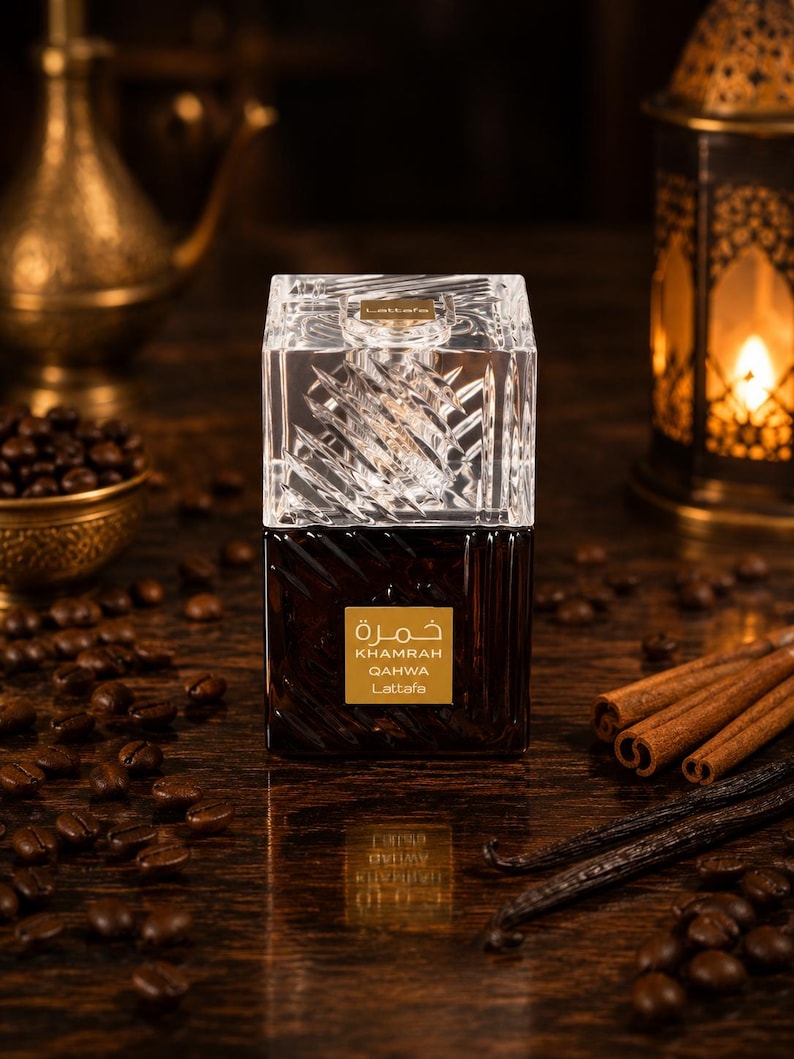 May include: A square glass perfume bottle with a clear, textured crystal-like cap and a dark brown base. The label features the text "KHAMRAH QAHWA Lattafa" in white and gold lettering, with Arabic script above the product name.