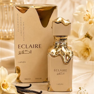 May include: A beige perfume bottle and its matching rectangular box, both labeled Eclaire Lattafa. The bottle and box feature a metallic gold drip design at the top. The packaging displays 100ml and 3.4 fl. oz. text. The bottle has a gold cap.