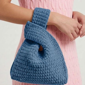 May include: A blue, textured, knotted handbag with a handle. The bag is made of a thick, woven material. The bag is held by a person wearing a pink dress.