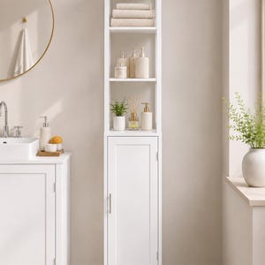 Pode incluir: Um armário de casa de banho branco, alto e estreito, com uma prateleira aberta na parte superior com três toalhas bege empilhadas e vários frascos de produtos de higiene, e uma secção inferior com uma porta e um puxador vertical prateado.