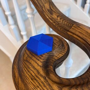 May include: A vibrant blue, geometric object rests on a richly grained, dark wooden handrail. The handrail curves gracefully, showcasing the natural wood pattern. The background features a white staircase with decorative balusters.