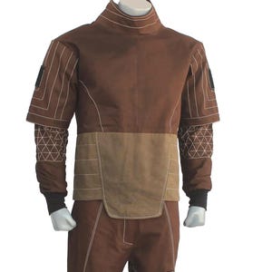 May include: A brown two-piece outfit consisting of a high-neck short-sleeve top with a lighter brown midsection and matching trousers. The garment features white contrast stitching, black sleeve cuffs, and black rectangular accents on the sleeves and legs.
