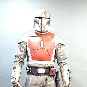 May include: A Mandalorian warrior costume. The outfit includes a helmet, chest armour, and protective elements in grey, red, and brown. The boots are brown, and the costume features a utility belt and holster. Measurements are in cm and kg.