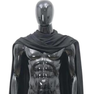 May include: A black mannequin with a glossy finish, wearing a black cape. The mannequin has a muscular physique and is standing against a white background. The cape drapes over the shoulders and arms.