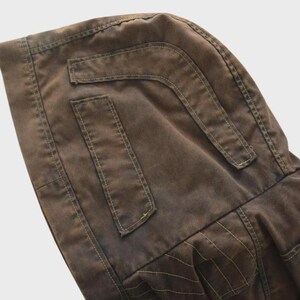 Puede incluir: Primer plano de una chaqueta con capucha marr&oacute;n. La chaqueta presenta dos bolsillos rectangulares y una capucha. Las costuras son visibles y la tela tiene un aspecto ligeramente desgastado. La chaqueta est&aacute; hecha de un material duradero.