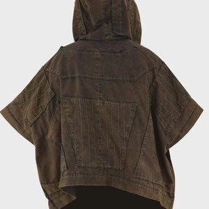 Puede incluir: Chaqueta con capucha marr&oacute;n con mangas cortas. La chaqueta presenta m&uacute;ltiples bolsillos y detalles de costura verticales en la espalda y las mangas. La prenda tiene un corte asim&eacute;trico &uacute;nico y un ajuste relajado.