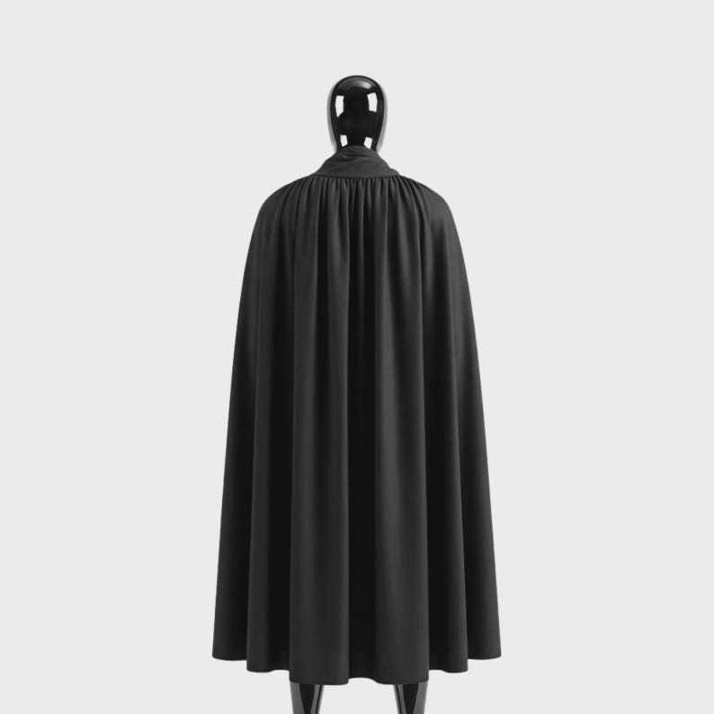May include: A black cape with a high collar, displayed on a mannequin. The cape is made of a flowing fabric, with vertical folds adding texture. The garment is a solid black color, suitable for costumes or formal wear.