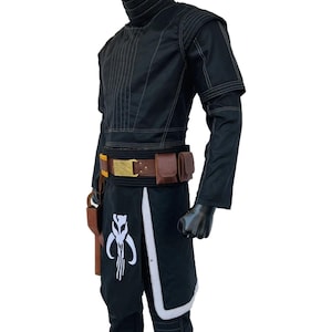 May include: Black costume with white stitching and accents. The outfit includes a high-collared jacket, a belt with pouches, and a skirt-like piece with a white emblem. A holster is attached to the belt. The costume is displayed on a mannequin.