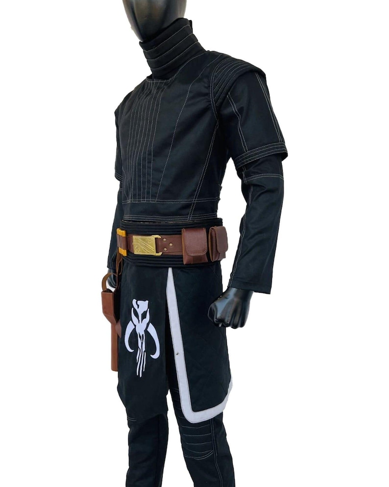 May include: Black costume with white stitching and accents. The outfit includes a high-collared jacket, a belt with pouches, and a skirt-like piece with a white emblem. A holster is attached to the belt. The costume is displayed on a mannequin.