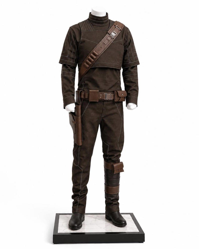 May include: A brown costume displayed on a mannequin. The outfit includes a high-collared top, pants, and a belt with pouches. A brown leather strap crosses the chest. The costume is accented with white stitching and includes a holster and leg wraps. Black boots complete the look.