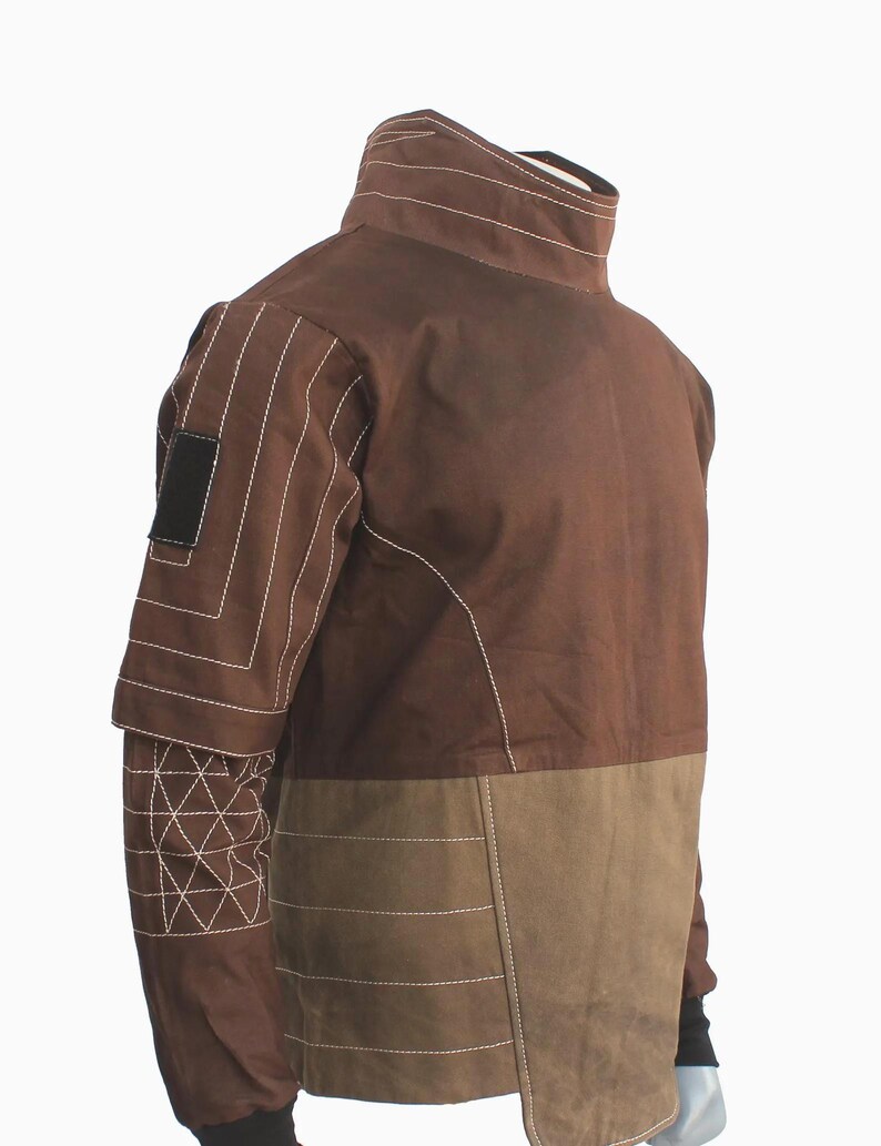 May include: A brown jacket featuring a high collar, long sleeves with white geometric stitching, and a rectangular black patch on the upper arm. The torso is divided into a dark brown upper section and a lighter brown lower section with horizontal stitching.