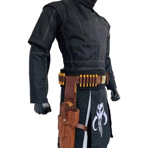 May include: Black costume with white stitching, featuring a high collar and a belt with gold-coloured details. A brown leather holster is attached to the belt. The costume includes a black skirt with a white emblem.