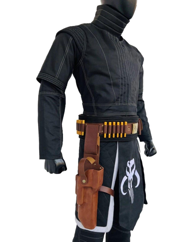 May include: Black costume with white stitching, featuring a high collar and a belt with gold-coloured details. A brown leather holster is attached to the belt. The costume includes a black skirt with a white emblem.